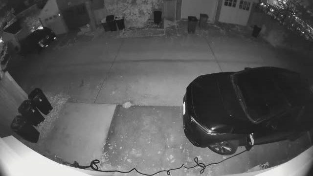 A car parked toward the right edge of the pad at night, the charger cable lying across the ground