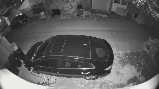 The alley at night in infrared: a dark SUV on the parking pad with the charger cable on the ground beside it